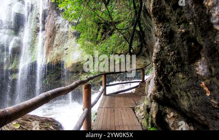 Ein hölzerner Pfad schlängelt sich durch einen lebhaften tropischen Wald und führt die Besucher zu einem atemberaubenden Wasserfall. Umgeben von üppigem Grün, der Klang von c Stockfoto