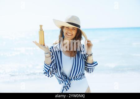 Lächelnde, moderne Frau mittleren Alters am Meer mit spf. Stockfoto