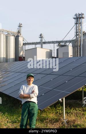 Farmerin mit digitalem Tablet auf einem modernen Bauernhof mit Solarpaneelen. Landwirtschaftliche Silos im Hintergrund. Stockfoto