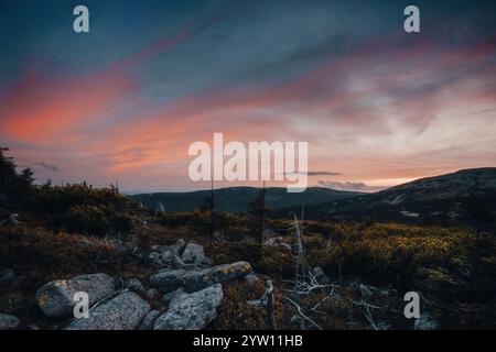 Ein atemberaubender Sonnenuntergang entfaltet sich über einem malerischen felsigen Hügel mit wunderschönen Bäumen, die die Szene im Vordergrund umrahmen Stockfoto