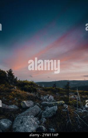 Ein atemberaubender Sonnenuntergang entfaltet sich über einem malerischen felsigen Hügel mit wunderschönen Bäumen, die die Szene im Vordergrund umrahmen Stockfoto