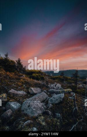 Ein atemberaubender Sonnenuntergang entfaltet sich über einem malerischen felsigen Hügel mit wunderschönen Bäumen, die die Szene im Vordergrund umrahmen Stockfoto
