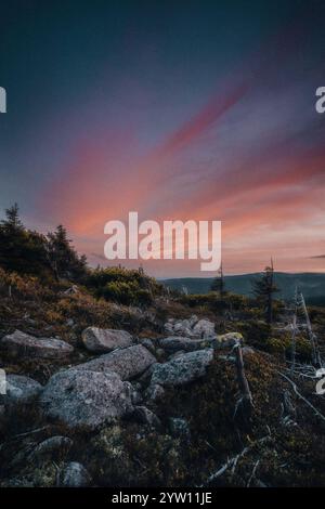 Ein atemberaubender Sonnenuntergang entfaltet sich über einem malerischen felsigen Hügel mit wunderschönen Bäumen, die die Szene im Vordergrund umrahmen Stockfoto
