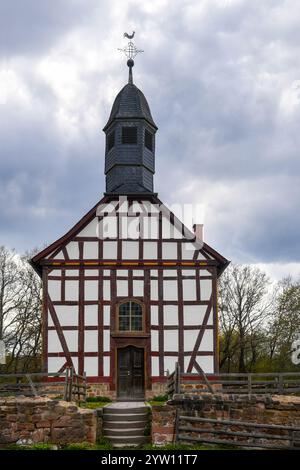 Eine historische Fachwerkkirche mit einem Schieferdach und einem kleinen Glockenturm, umgeben von einem rustikalen Steinzaun und Grün, Stockfoto