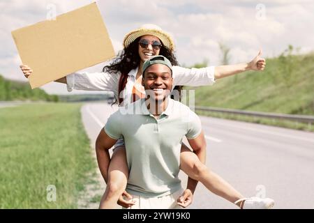 Die ganze Länge eines glücklichen multirassischen Paares per Anhalter, versucht, das Auto mit leerem Pappschild anzuhalten, Mockup Stockfoto