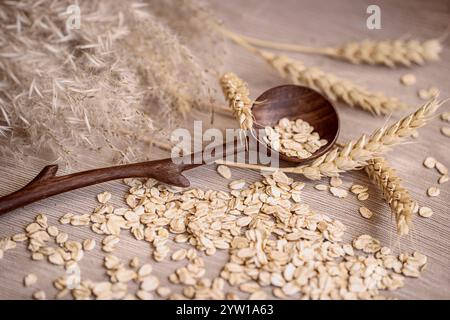 Holzlöffel hält Hafer, Körner, Weizenstiele auf Holzoberfläche, natürliche Lebensmittel, gesunde Rezepte Konzept Stockfoto