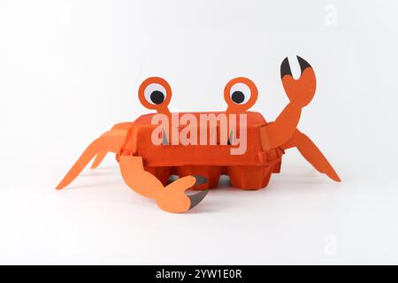 Handgemachte Krabbenhandwerk aus bemaltem orangenem Eierkarton mit Papierklauen und Augen auf weißem Hintergrund. Studio-Fotografie. Sommerkreation A Stockfoto