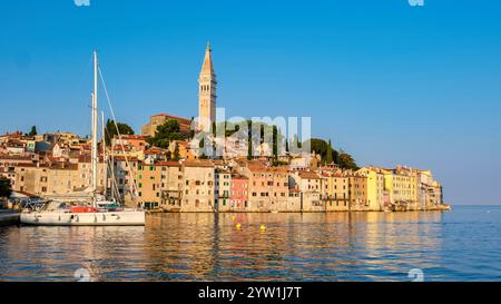 Während die Sonne über Rovinj Kroatien untergeht, ist der Himmel in warmen Tönen gemalt, die ein goldenes Leuchten auf die malerische Uferpromenade werfen. Farbenfrohe Gebäude säumen die Stockfoto