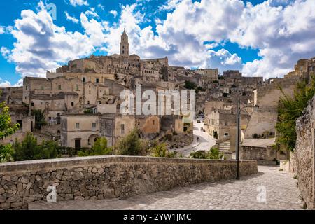 Wandern Sie durch die historischen Gassen von Matera in Apulien, Italien, wo sich alte Steinbauten gegen einen atemberaubenden Himmel erheben, der im Sommer mit flauschigen Wolken geschmückt ist Stockfoto