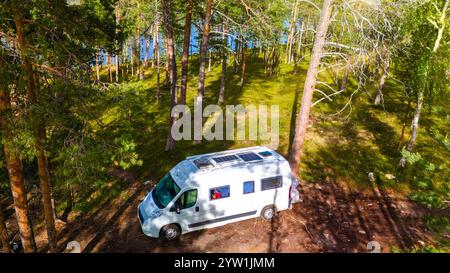 Ein weißer Wohnmobil parkt auf einer Rodung inmitten eines dichten Waldes im finnischen Lappland. Sonnenlicht filtert durch die Bäume und wirft schattige Schatten auf t Stockfoto