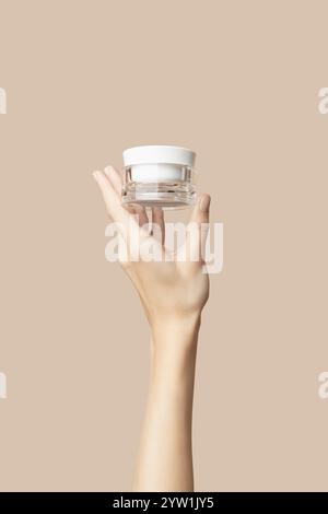 Eine Frauenhand, die ein weißes Kosmetikglas auf beigefarbenem Hintergrund hält. Pflegeprodukte Stockfoto