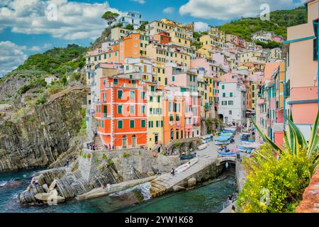 Farbenfrohe Gebäude schmiegen sich an die zerklüfteten Klippen von Cinque Terre, während Fischerboote sanft im Hafen schweben. Riomaggiore in Cinque Terre, Italien Stockfoto