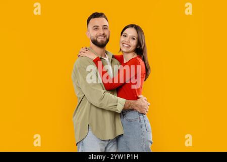Das junge Paar drückt Liebe und Zuneigung vor einem hellgelben Hintergrund aus Stockfoto