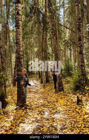 Zwei Menschen laufen durch einen Wald, einer von ihnen blickt hinter einem Baum hervor. Die Szene ist friedlich und ruhig, da das Paar seine Zeit genießt Stockfoto