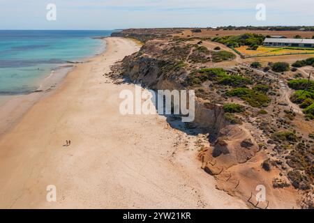 Blick auf zwei kleine Figuren, die an einem Strand unter zerklüfteten Küstenklippen am Port Willunga in Adelaide, South Australia, spazieren. Stockfoto