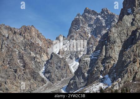 Raue, zerklüftete Berggipfel stehen unter klarem blauen Himmel. Der Gipfel ist teilweise mit Schnee bedeckt, was auf eine hohe Höhe und niedrige Temperaturen hinweist. Abwesenheit von Stockfoto