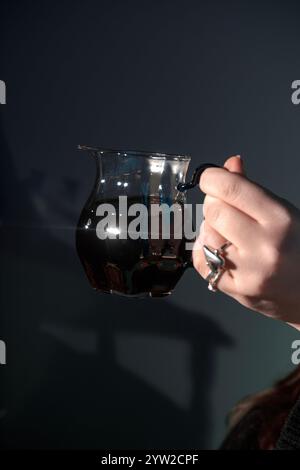 Die Nahaufnahme einer Hand, die einen Glaskrug mit reichhaltiger Flüssigkeit hält, unterstreicht das elegante Design und die Handwerkskunst Stockfoto