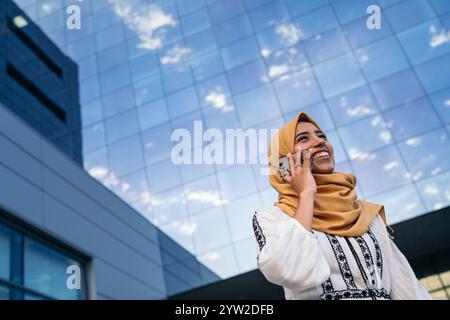 Muslimische Geschäftsfrau in Hijab, die vor einem modernen Bürogebäude telefoniert Stockfoto