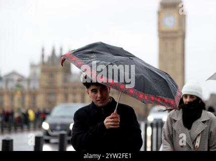 London, Großbritannien. Dezember 2024. Die Leute laufen am 8. Dezember 2024 auf der Westminster Bridge in London, Großbritannien. Zehntausende von Häusern wurden ohne Strom gelassen, Bahn- und Luftverkehr wurden gestört und Sportveranstaltungen in ganz Großbritannien wurden am Samstag abgesagt, als der Sturm Darragh zuschlug. Quelle: Li Ying/Xinhua/Alamy Live News Stockfoto