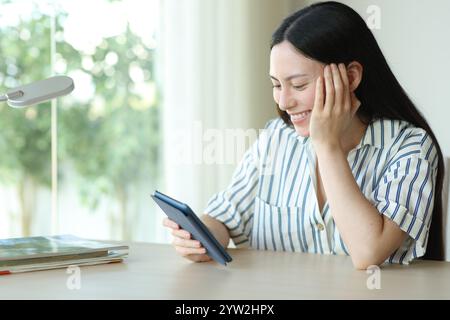 Glückliche asiatische Frau, die eBook liest, sitzend in einem Zimmer zu Hause Stockfoto