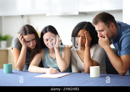Vier traurige interrassische Freunde, die in der Küche zu Hause einen schlechten Vertrag überprüfen Stockfoto