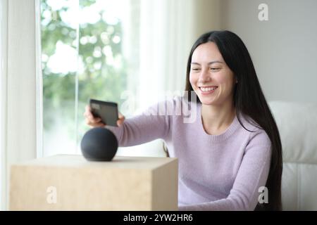 Glückliche asiatische Frau, die zu Hause Telefon und virtuellen Lautsprecher koppelt Stockfoto