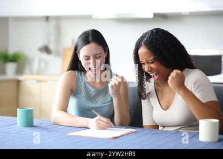 Aufgeregtes interrassisches Paar unterzeichnet Vertrag, um Erfolg in der Küche zu Hause zu feiern Stockfoto