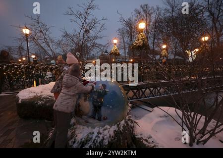 Nicht exklusiv: CHARKIW, UKRAINE - 7. DEZEMBER 2024 - zwei Mädchen erkunden während der Weihnachtszeit eine große Kugel, Charkiw, Nordostukraine. Stockfoto