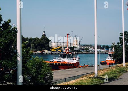 Orangene Schlepper legen an einer Uferpromenade in der Nähe des historischen Leuchtturms und der maritimen Gebäude an. Danzig Hafenszene. Danzig, Polen - 19. Mai 2024 Stockfoto