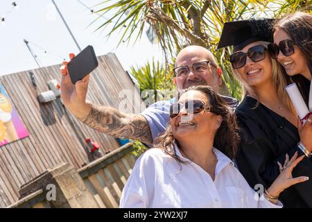 Eine fröhliche Gruppe von vier Personen, die an einem sonnigen Tag ein Selfie machen, mit zwei Einzelpersonen in Graduiertenmützen, die einen Meilenstein feiern, Bournemouth, Dorset UK Stockfoto