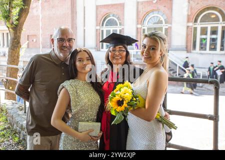 Lächelnde vierköpfige Gruppe feiert einen Abschlussfeiertag vor einem Backsteingebäude mit großen Fenstern, Bournemouth, Dorset UK Stockfoto