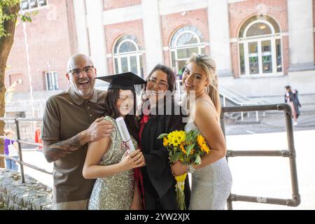 Lächelnde Familie feiert den Abschluss einer jungen Frau vor einem Backsteingebäude mit großen Fenstern, Bournemouth, Dorset UK Stockfoto