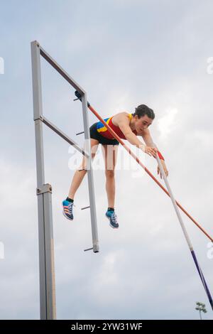 Weibliche Athletin in der Luft, die bei einem Outdoor-Leichtathletik-Event mit bewölktem Himmel im Hintergrund über die Bar springt Stockfoto