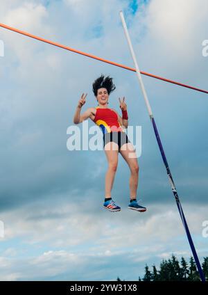 Weibliche Athletin räumt die Bar während eines Stabhochsturzes unter teilweise bewölktem Himmel. Stockfoto