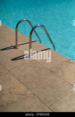 Die Schwimmbadleiter aus Edelstahl führt an einem sonnigen Tag in klares blaues Schwimmbadwasser, Portugal Stockfoto