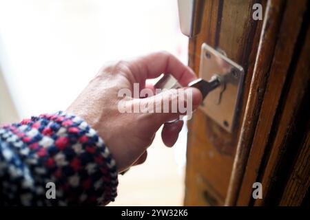 Nahaufnahme einer Hand, die einen Schlüssel in ein hölzernes Türschloss einführt. Stockfoto