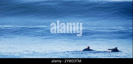 Zwei Surfer paddeln mit einer riesigen Welle im Hintergrund zur Besetzung. Stockfoto