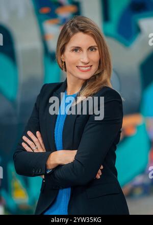 Selbstbewusste Geschäftsfrau in blauem Oberteil und schwarzem Blazer mit überkreuzten Armen vor einer farbenfrohen Graffiti-Wand. Stockfoto