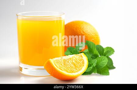 Leuchtender Orangensaft füllt ein Glas neben einer ganzen Orange, die in Scheiben geschnitten wird, und Minzblätter verleihen in einer hellen Umgebung einen frischen Touch. Stockfoto