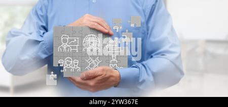 Ein Geschäftsmann in einem blauen Hemd hält ein digitales Puzzle mit verschiedenen geschäftsbezogenen Ikonen. Das Bild stellt Teamarbeit, Strategie und Geschäftspläne dar Stockfoto