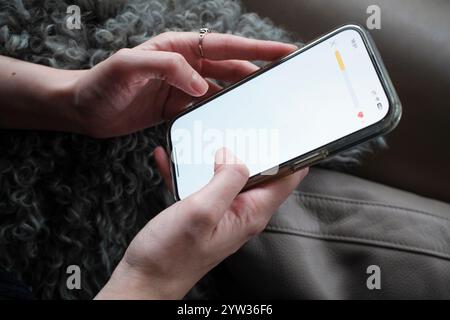 Nahaufnahme von Frauenhänden, die ein Smartphone mit einem leeren Bildschirm vor einem grauen gestrickten Hintergrund halten. Stockfoto