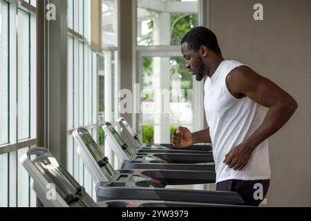 Junger, kurzes, lockiges schwarzes Haar, mit Schnurrbart und Bart, der im Fitnessstudio auf einem Laufband läuft. Stockfoto