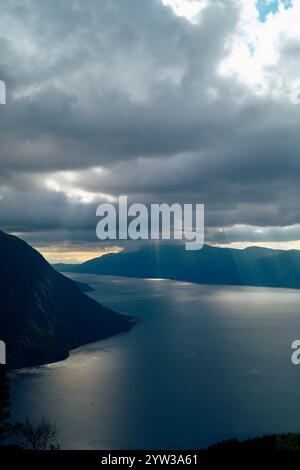 Sonnenstrahlen brechen durch die Wolken über einem ruhigen Fjord, umgeben von Bergen, Romsdalfjord, Norwegen Stockfoto