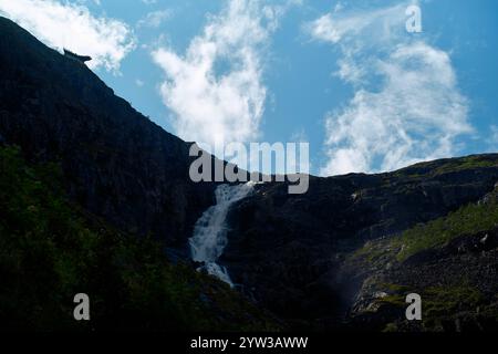 Ein kaskadenförmiger Wasserfall fließt unter einem blauen Himmel mit weißen Wolken über eine zerklüftete Klippe, Trollvegen, Norwegen Stockfoto