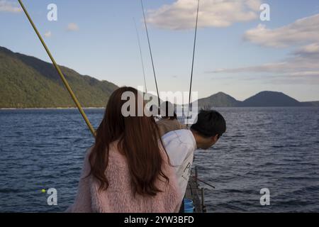 Mädchen mit rotem Haar und rosa Jacke, Fischer mit Angelruten auf einem Steg, Berge im Hintergrund, Shikotsu-Toya Nationalpark, Shikotsu See, Stockfoto