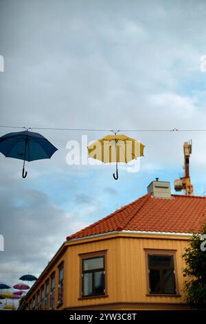 Bunte Regenschirme hängen an einem bewölkten Himmel über einem Stadtgebäude in Trondheim, Norwegen Stockfoto