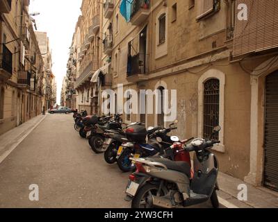 Eine enge Straße gesäumt von Motorrädern auf dem Bürgersteig und klassischen Apartmentgebäuden mit Balkonen in einer europäischen Stadt, Barcelona, Spanien Stockfoto