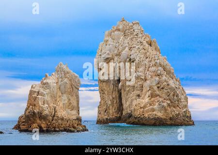 Eine große Felsformation befindet sich an der Küste des Ozeans. Der Himmel ist blau und bewölkt. Die Felsen sind weiß und grau Stockfoto