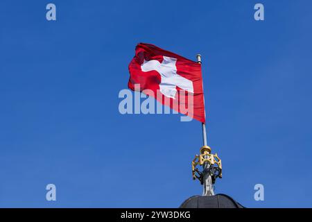 Die Nationalflagge der Schweiz weht im Wind gegen einen blauen Himmel, Schweizer Flagge auf dem Kirchturm von Grossmunster. Stockfoto