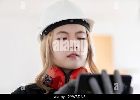 Bauarbeiter mit weißem Schutzhelm und Ohrenschützern mit Smartphone. Stockfoto